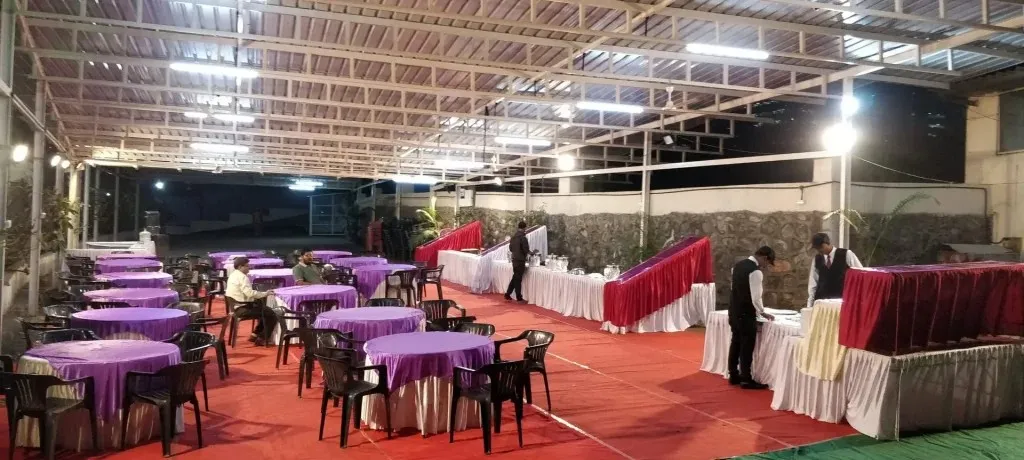 Open-air banquet hall with purple draped tables and uniformed staff setting up for an event at Kapila Resorts Kharadi Pune